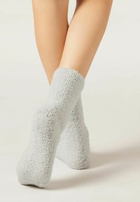 Hellgraue, fuzzy Socken mit weicher Textur, ausgestattet mit einem gerippten Oberteil und gepunkteten rutschfesten Griffen auf der Sohle für besseren Halt.