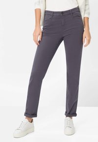 Tætsiddende, mørkegrå bomuldsbukser med synlige forlommer, bæltestropper og lukning med knap; båret med hvide sneakers.