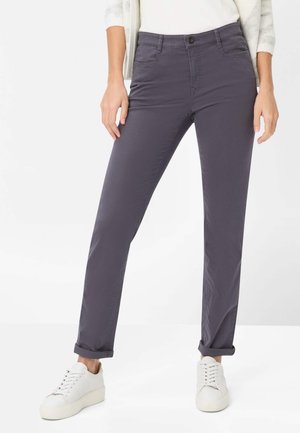 Tætsiddende, mørkegrå bomuldsbukser med synlige forlommer, bæltestropper og lukning med knap; båret med hvide sneakers.