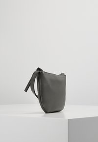Borsa a mano in pelle grigia con una texture liscia, dal design minimalista e con chiusura a zip superiore. Presenta un manico corto su un lato.