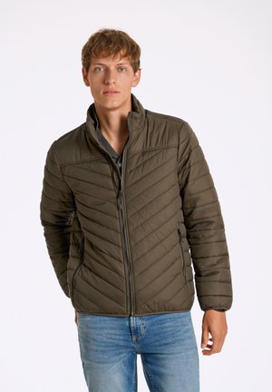 Chaqueta acolchada de color verde oliva con cierre de cremallera en la parte delantera, cuello alto, patrón de acolchado diagonal y dos bolsillos laterales, llevada sobre una camiseta gris.
