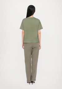 Olivegrünes T-Shirt mit kurzen Ärmeln, Rundhalsausschnitt, kombiniert mit passenden olivegrünen Hosen, die eine lässige Passform und eine weiche Textur aufweisen.