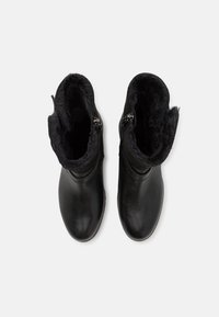 Botas de tobillo de cuero negro con forro de piel sintética, que presentan un borde superior curvado y acentos de cremallera lateral. Textura suave y diseño de punta redonda.