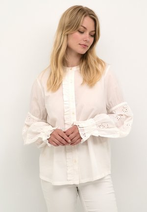 Balta blusa su raukšlėtu priekiu ir organzos tipo rankovėmis. Yra akyčių detalės ant rankogalių. Lengva medžiaga. Atsitiktinė išvaizda.