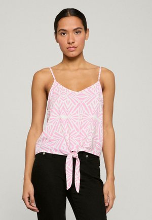 Top en satin rose avec des motifs géométriques blancs, bretelles fines et ourlet noué à l'avant, associé à un pantalon noir ajusté.