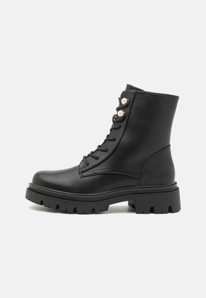 Black leather ankle boots with a rounded toe, lace-up design, and decorative rose gold eyelets. Thick, rugged rubber sole with treads.