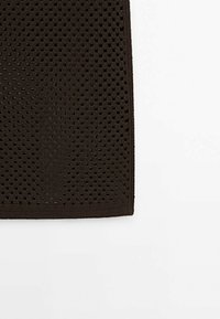 Dunkelbrauner Stoff mit sechseckigem Ausschnittmuster und einer strukturierten Oberfläche, mit einem eingefassten Rand, geeignet für verschiedene Anwendungen.