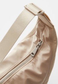 Borsa a spalla beige chiaro in nylon con una superficie liscia, dotata di una cerniera argentata e di una tracolla piatta e regolabile.