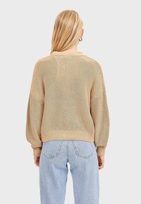 Beżowy sweter dzianinowy o luźnym kroju, z prążkowanymi mankietami i dołem. Teksturowany splot posiada swobodny dekolt i opuszczone ramiona.
