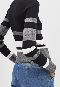 Czarnobiały, prążkowany sweter w paski o różnej szerokości, z teksturowanej tkaniny i dopasowanym kroju, zestawiony z niebieskimi dżinsami.