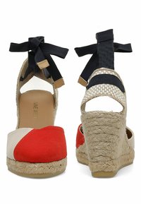 Espadrilles compensées en toile rouges et beiges avec des liens de cheville en ruban noir, talon en jute et dos ouvert pour la respirabilité.