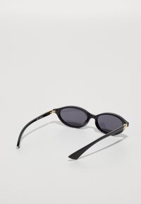 Black oval sunglasses with dark lenses, glossy plastic frames, gold accents near the hinges, and sleek, elongated arms.