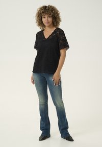 Black lace top with short, scalloped sleeves and a V-neckline, paired with flared blue jeans and black pointed-toe shoes.