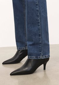 Botines de cuero negro con punta afilada y tacón bajo, combinados con unos jeans de mezclilla azul de corte recto y dobladillo deshilachado.