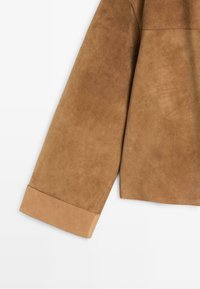Manche de veste en daim marron avec un détail de poignet plié, mettant en avant une texture douce et des coutures lisses sur un fond uni.