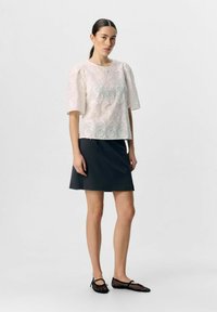 Haut à manches courtes brodé en rose clair, associé à une jupe sombre. Il présente des motifs floraux et un col rond, fabriqué en tissu texturé.