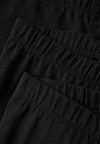 Close-up van drie opgestapelde zwarte elastische taillebanden op zachte stof, met gedetailleerd stikwerk en gerimpelde textuur.