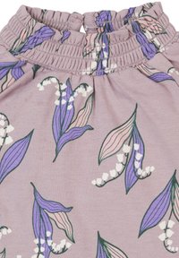 Lila Stoff mit einem Blumenmuster, das grüne und pinke Blätter sowie weiße Maiglöckchenblüten zeigt. Gehüpfte Kragen mit Knopfverschluss.