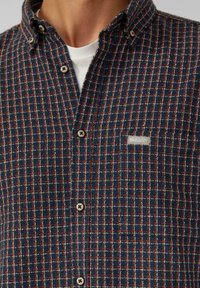 Marineblauw en rode geblokte button-up shirt van een gestructureerde stof, met een voorke pocket en knoopsluiting. Geaccentueerd met lichtgekleurde stiksels.