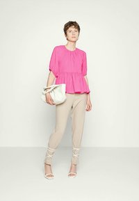 Top peplum em fúcsia com tecido texturizado, calças bege justas, sandálias brancas com tiras e uma mala de couro branca. Design simples e moderno.