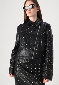 Črna usnjena jakna s srebrnimi nitnimi detalji, z zadrgo spredaj, stranskimi žepe in pasom. Eleganten dizajn s ovratnikom.