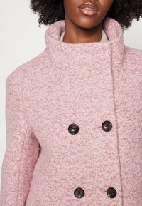 Růžový kabát z vlněné směsi s texturovaným povrchem, širokým límcem a dvouřadým zapínáním na tmavé knoflíky. Minimalistický design a struktura.