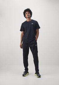 Zwart sportief T-shirt met klein logo, gecombineerd met zwarte joggingbroek met gestructureerde panelen en zwarte sneakers met gele zolen.