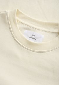 Crèmekleurige sweatshirt met een ronde halslijn en subtiele ribbeltextuur. Etiket leest "Matinique." Zacht materiaal, minimalistisch ontwerp.
