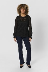 Blusa in pizzo nero con motivo intricato e maniche lunghe, abbinata a jeans flair blu scuro e scarpe nere con punta.
