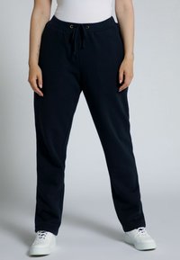 Námorní jogger kalhoty vyrobené z měkkého materiálu, s elastickým pasem na šňůrku, bočními kapsami a volným střih, doplněné o bílé tenisky.