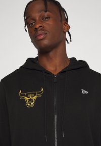 Sudadera con cremallera negra con logo de toro amarillo y logo de marca bordado en blanco. Confeccionada en tela suave con un corte holgado y capucha con cordón.