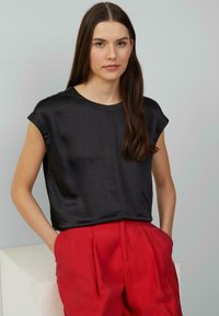 Haut noir à manches courtes avec une coupe décontractée et une texture en satin, associé à un pantalon rouge taille haute. Détails minimalistes et décolleté rond.