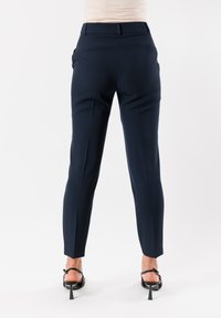Pantaloni slim-fit blu navy con un tessuto liscio, fronte piatto e tasche laterali. Presentano una vita su misura e gambe affusolate.