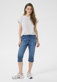 Ljust grå kortärmad skjorta med uppvikta ärmar, kombinerad med blå knälånga jeans med en lätt frans. Bärs med vita sportskor.