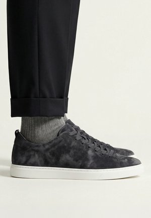 Black cuffed pants, gray ribbed socks, and dark gray suede sneakers with white soles on light background.