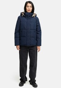 Mörkblå vadderad jacka med huva, med dragskor, kviltad design och sidofickor, kombinerad med svarta vida jeans och svarta skor.