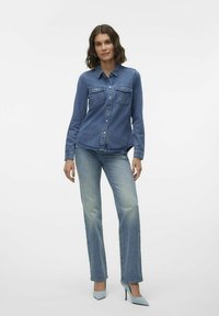 Denimskjorte med to frontlommer og knappelukking, kombinert med lyseblå rette bukser og lyseblå høye hæler.