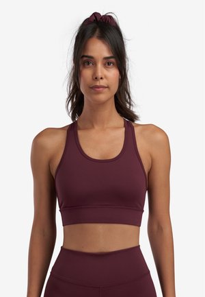 Maroon sports bra with a fitted design, wide shoulder straps, and a smooth texture. Seam detailing along the edges for added structure.
