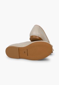 Pantofi din piele bej cu vârf ascuțit și toc mic. Textură netedă și talpă solidă de culoare bej cu inscripția "MADE IN SPAIN" și mărimea tipărită pe partea de jos.