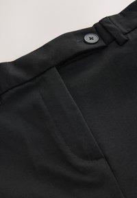 Pantaloni neri con una texture liscia, dotati di chiusura con bottone e tasche laterali. Design pulito con vestibilità su misura e dettagli di cucitura minimali.