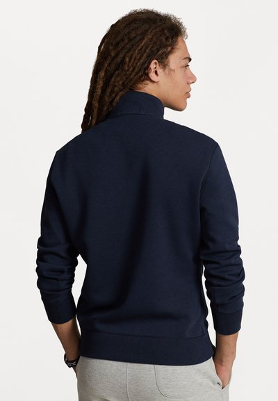 Navy sweatshirt med høy krage, lange ermer med ribbede mansjetter og en glatt tekstur. Sett fra baksiden med et minimalistisk design.