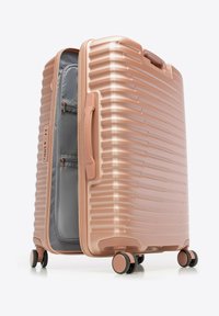 Valigia rigida colore rosa oro con superficie testurizzata, quattro ruote girevoli, maniglia laterale, cerniera parzialmente aperta che rivela un interno grigio con tasche.