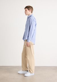 Camicetta con righe blu e bianche, pantaloni beige larghi e sneakers bianchi, vista di lato. Tessuto liscio, vestibilità rilassata.