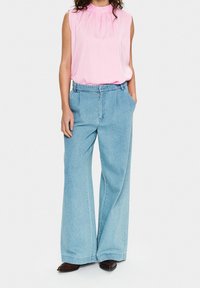 Różowy top bez rękawów z marszczonym dekoltem, zestawiony z wysokim stanem, szerokimi, jasnoniebieskimi jeansami z bocznymi kieszeniami i luźnym krojem.
