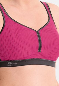 Różowy stanik sportowy z teksturowanym, perforowanym wzorem. Posiada czarną lamówkę i zamek błyskawiczny z przodu oraz wspierający pas pod biustem.