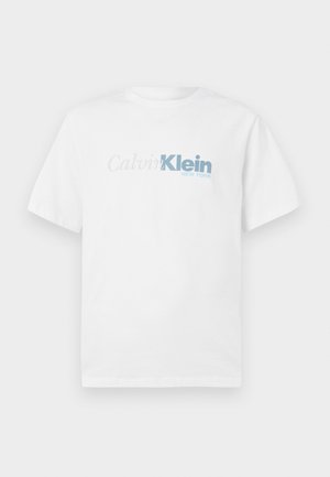 Valkoinen lyhythihainen T-paita, jossa on "Calvin Klein New York" -logo vaaleanharmaana ja sinisenä keskitettynä etuosassa.