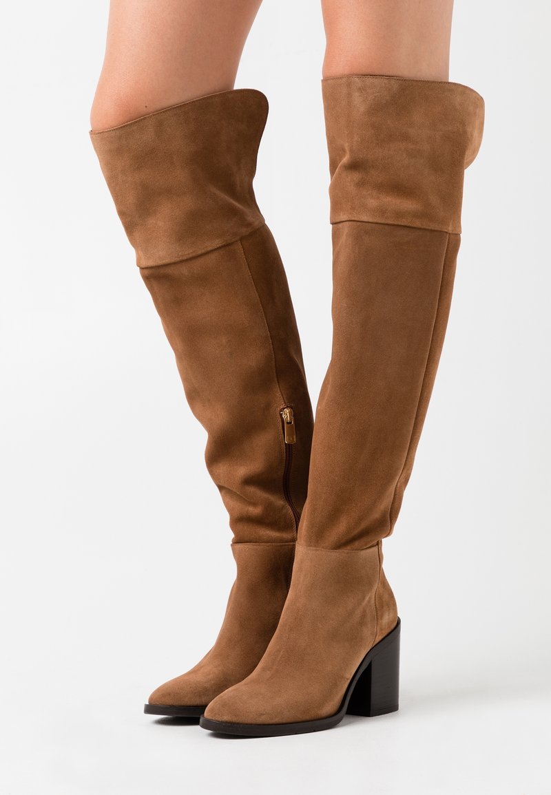 Bruine suede laarzen tot boven de knie met een spitse neus en een blokhak. Beschikt over een rits aan de binnenzijde en een omgevouwen bovenrand.