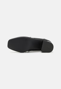 Chaussure en cuir noir avec un bout carré et un petit talon. La semelle extérieure possède une texture lisse et des nervures discrètes pour une meilleure adhérence.