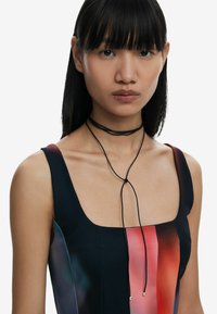 Choker-style necklace with black cords, featuring silver accents, worn with a sleeveless dress displaying a gradient of red and black hues.