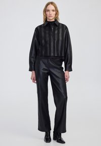 Czarna skórzana kurtka w stylu cropped z pionowymi paskami, zapięciem na guziki i kołnierzem, w połączeniu z czarnymi skórzanymi spodniami o wysokim stanie i botkami sięgającymi kostek.